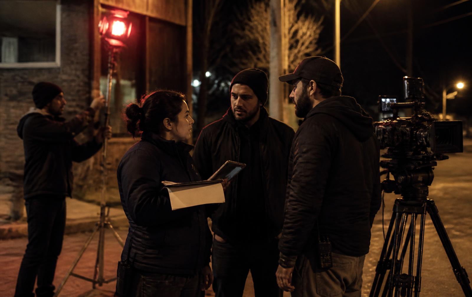 Small film crew discussing the schedule beside a cinema camera at night